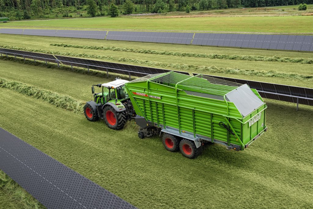tractor with trailer driving through field with solar panels