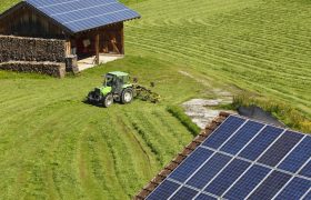 Tractor in field with solar panels on barns.